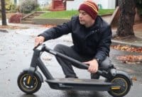 Man crouching with a folded Ninebot Max electric scooter