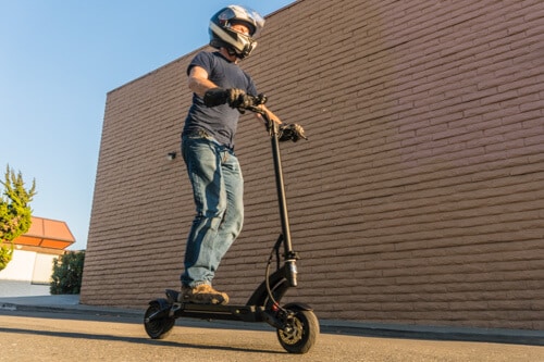 Man riding Kaabo Mantis 8 electric scooter, wearing helmet and gloves