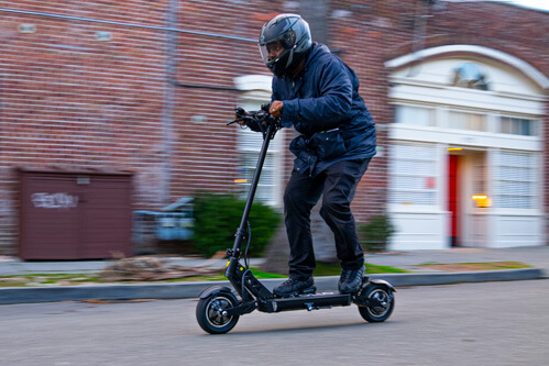 Apollo Ghost electric scooter - man riding scooter to left of frame, going fast, full view