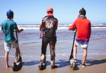 Three men standing on electric scooters at the waves of the Pacific Ocean