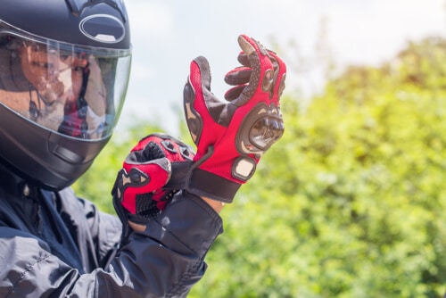 man wearing motorcycle helmet and securing gloves, Source: Shutterstock, ID: shutterstock_1099369940