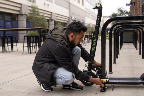 Man locking Inokim Light 2 electric scooter to a biek rack