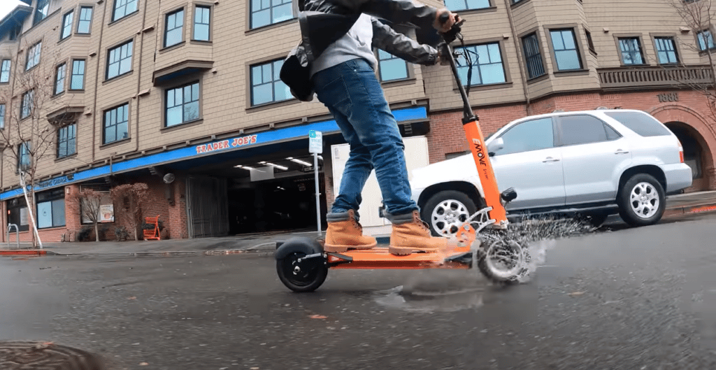 Man rides an EMOVE Cruiser electric scooter through a puddle on the street 